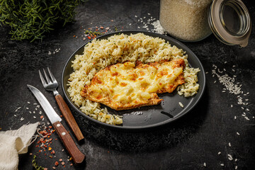 Grilled hawaiian chicken with cheese, ananas and boiled rice served on a black plate