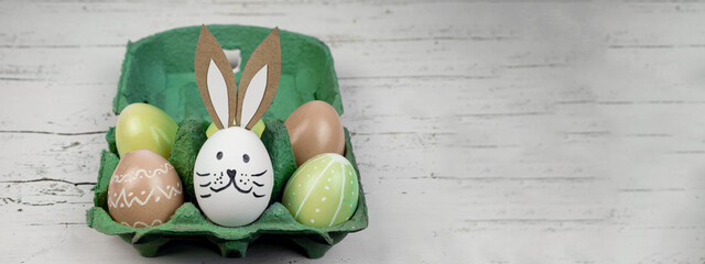 Happy Easter background banner panorama greeting card -Close-up from colorful painted eggs and easter bunny in green egg carton on rustic white vintage shabby wooden table