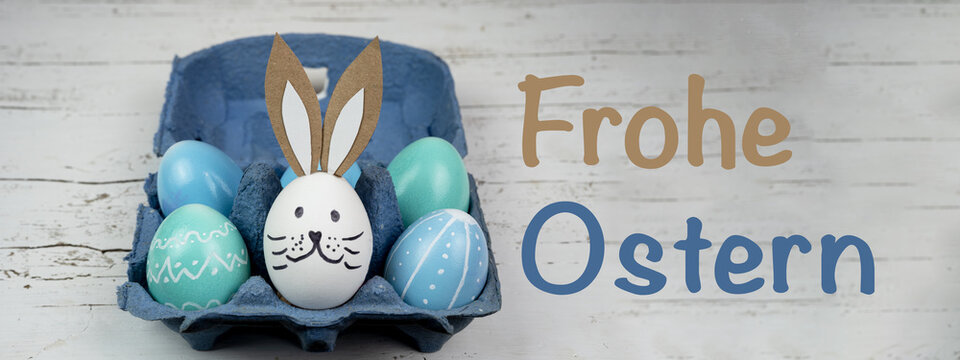Frohe Ostern Hintergrund Banner Panorama Gru&szlig;karte - Nahaufnahme von bunten bemalten Eiern und Osterhase in blauem Eierkarton auf rustikalem wei&szlig;en Vintage shabby Holztisch