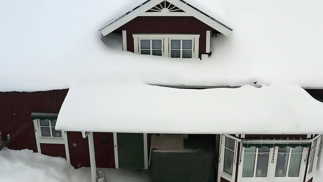 Video looks like 3D rendered cartoon of red wooden traditional Swedish house covered by much snow in countryside. Fly away and up, snowing, pine trees at background. Cartoon effect applied to footage