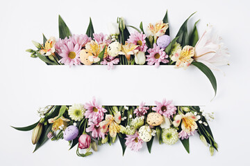 Creative layout made with arranged flowers and colorful Easter eggs on bright white background. Minimal spring bloom concept. Women's day or valentines greeting card with copy space. Flat lay.