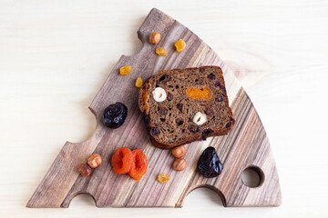 A piece of rye bread with dried fruits on a board, dried apricots, raisins, prunes and hazelnuts, top view.
