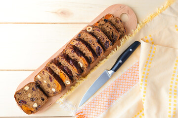 Freshly baked homemade bread with dried fruits, cut on a board and a knife on a wooden surface, top view.