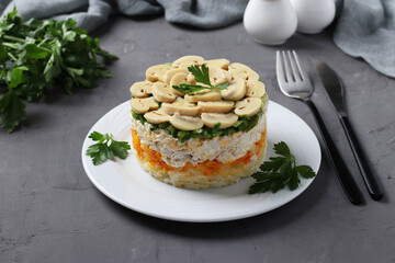 Puff salad with chicken, pickled mushrooms, potatoes and carrots on plate on grey background.