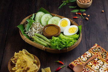 Pecel Sayur or Indonesian Vegetables salad with peanut sauce, served with peanut crackers. Dark mood photography concept. 