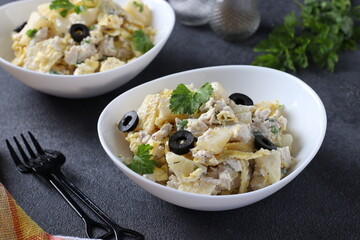 Salad with pineapple, baked chicken, omelette and black olives in white bowls on a dark gray background. Closeup