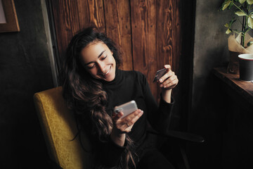 Young happy woman shopping online using her smartphone and credit card. 