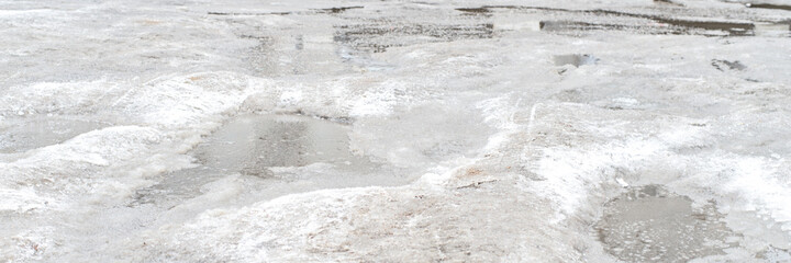 Puddles and ice on the asphalt. Uncleared city roads