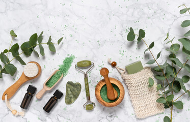 Obraz na płótnie Canvas Natural skin care and aromatherapy with eucalyptus essential oil bottle, bath salt, beauty jade roller, gua sha on marble background. Spa, wellness, massage, relaxation concept. Top view, copy space