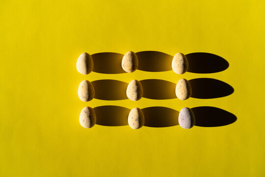nine chocolate colorful eggs on bright yellow background.