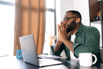 Serious focused African American businessman or freelancer working on an important project while sitting at his desk concentrated looks into a laptop, thinking about work