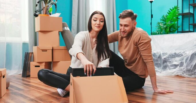 Couple move at new home take out unpack belongings from carton boxes holds frame looks at photo share memories feels happy. Buy first own property changes in life mortgage concept