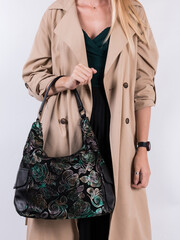 Woman in a beige raincoat with a black suede bag with a metallic flowers and leafs print