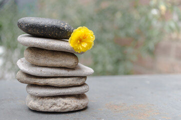 Stack of smooth gray stones and yellow flower on blurred background. Sea pebbles pile in nature.