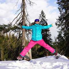 Bright snowboarder in ski suit jumping joyfully, recreation concept. Cheerful girl jumping in a star pose.