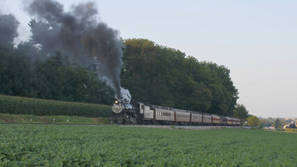 View of An Antique Restored Steam Locomotive Blowing Smoke and Steam Traveling Thru Farmlands and Countryside on a Sunny Summer Day