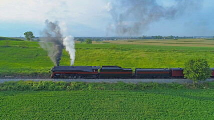 Fototapeta na wymiar Aerial View of An Antique Restored Steam Locomotive Blowing Smoke and Steam Traveling Thru Farmlands and Countryside on a Sunny Summer Day