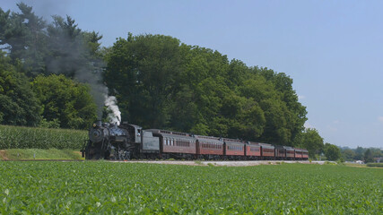 Fototapeta na wymiar View of An Antique Restored Steam Locomotive Blowing Smoke and Steam Traveling Thru Farmlands and Countryside on a Sunny Summer Day