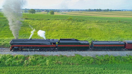 Aerial View of An Antique Restored Steam Locomotive Blowing Smoke and Steam Traveling Thru Farmlands and Countryside on a Sunny Summer Day