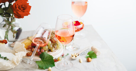 Rose wine in different wineglasses bottle on white table with grapes cheese, snacks bouquet of flowers. modern still life Rose Wine composition on light grey concrete background. Long Web banner
