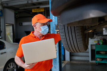 Caucasian male mechanic use laptop to check spec of car wheel on hydraulic lift