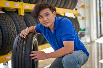 Asian male staff of car tire station service choose one tire from shelf list for customer car