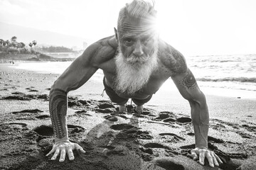 Age is just a number. In a healthy body, healthy mind. Senior man with white stylish beard doing push ups on the beach.