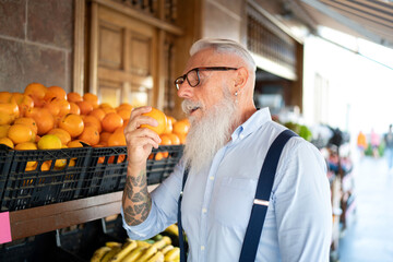 Handsome senior man with beard and eyeglasses choosing organic fruits in the grocery store, buying oranges for fresh juice.