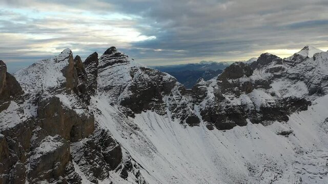 Aerial shot flying slowly backwards over a mountain ridge covered in snow and nice. Steep and drastic slopes and cliffs in secluded nature with no one around. Empty, quiet wilderness at high altitude.