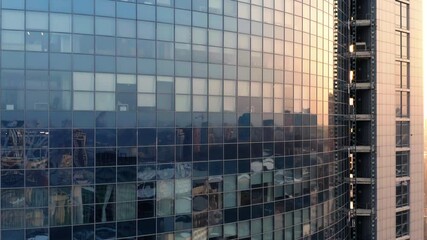 Aerial elevator shot of a modern glassed office skyscraper exterior with cityscape reflection in the windows at sunset or dawn