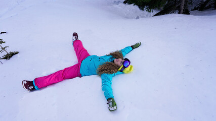 bright cheerful girl snowboarder lies on the snow in a pose of a star and smiling