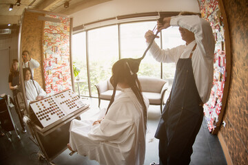 Asian male hairdresser make hairstyles for Asian female customers in modern beauty salons in Bangkok city.
