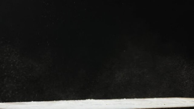 Loaf of fresh bread falls down on table shaking off white flour and rolls away on black background extreme closeup slow motion