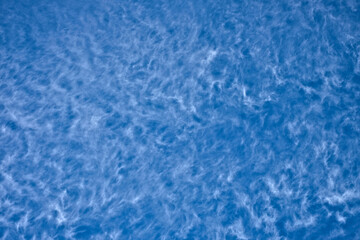 White fluffy cirrus clouds in vivid light blue sky.