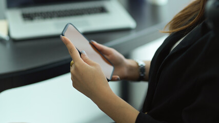Businesswoman in black suit hands holding mock up smartphone at workplace