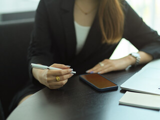 Businesswoman with pen in her hand working with smartphone and stationery