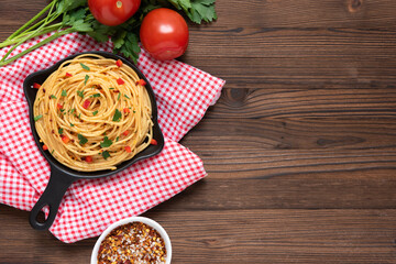 Pasta in a frying pan on a dark wooden background with vegetables. Top view.