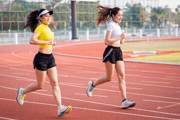 Obraz premium Two young Asian women in sports outfits jogging on running track in city stadium in the sunny morning to keep fitness and healthy lifestyle. Young fitness women run on the stadium track