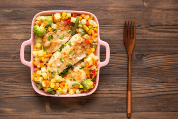 Homemade baked chicken with different seasonings and vegetables on a dark wooden background.