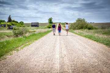 three grown people strolling down gravel road in the summer.