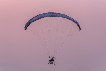 Silhouette of the Paramotor gliding and flying In the air through soft sunlight sky