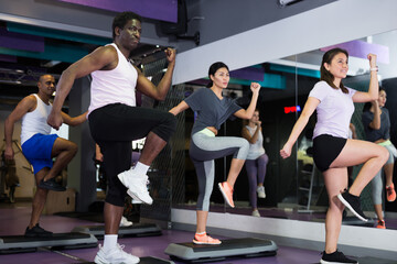 Concentrated athletic young adult people working out with aerobic steppers in gym