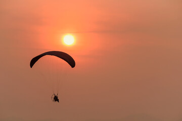 Silhouette of the Paramotor Gliding And Flying In The Air through soft sunlight sunset sky.