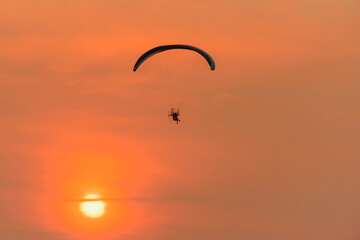 Silhouette of the Paramotor Gliding And Flying In The Air through soft sunlight sunset sky.