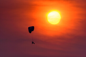 Silhouette of the Paramotor Gliding And Flying In The Air through soft sunlight sunset sky.