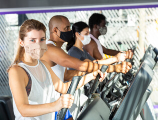Slim athletic people in protective masks running on treadmill in a fitness club