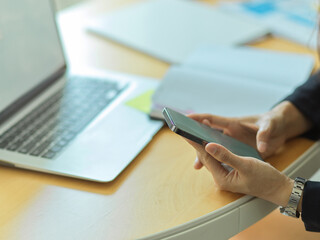 Businessman using smartphone in his hands on workspace with laptop and supplies