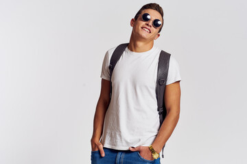man in sunglasses with a backpack on his back and in a white t-shirt on a light background cropped view of emotion