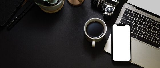 Top view of dark workspace with smartphone, laptop, coffee cup and copy space