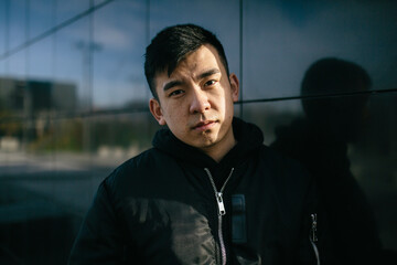 Portrait of a chinese man, wears urban clothing, looking at the camera with a serious expression....